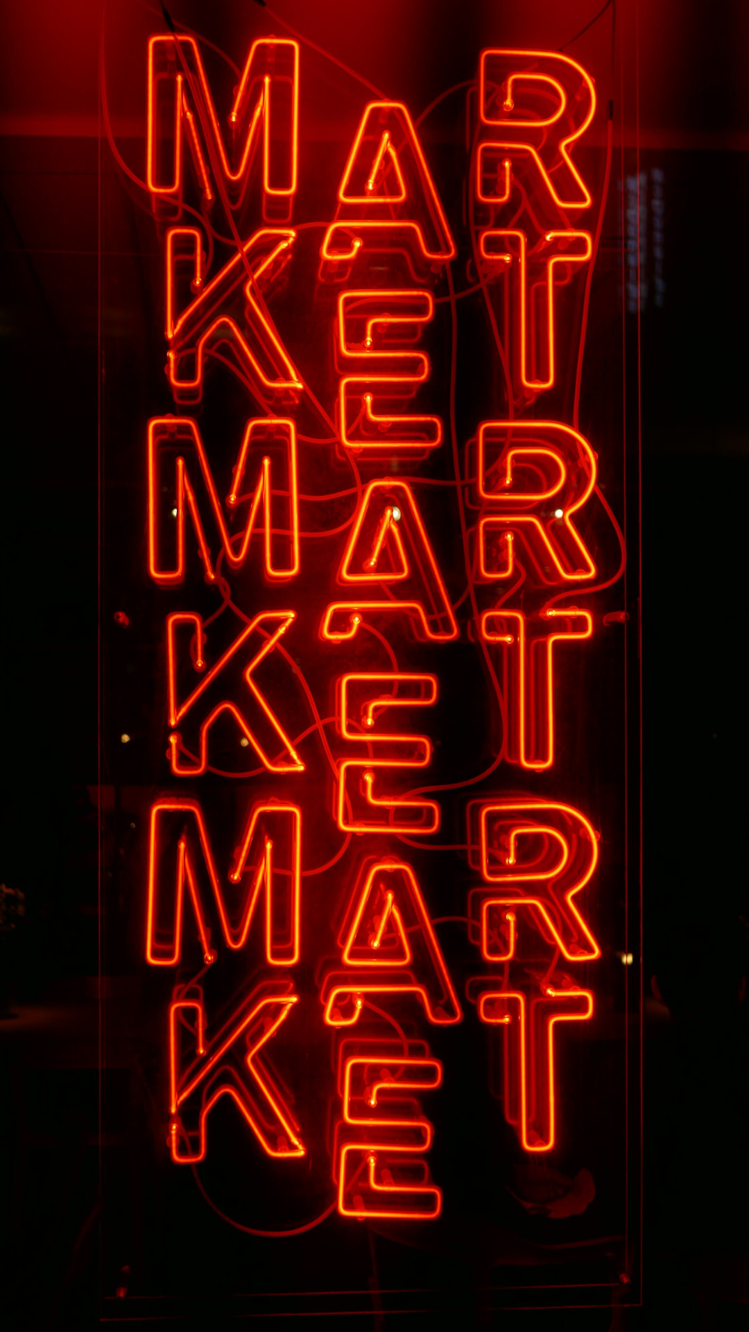Neon sign spelling MARKET repeated in red-orange tubes on a dark background